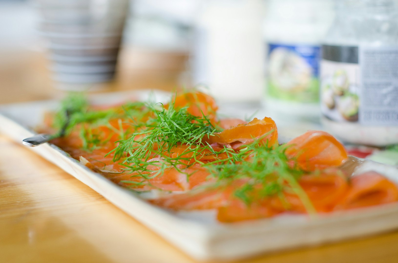 The image displays slices of cured or smoked salmon, commonly known as gravlax or lox, garnished with fresh dill on a rectangular serving plate