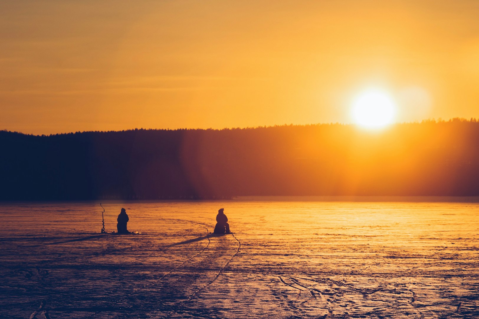 This image captures a tranquil moment of people ice fishing on a frozen lake during sunrise or sunset